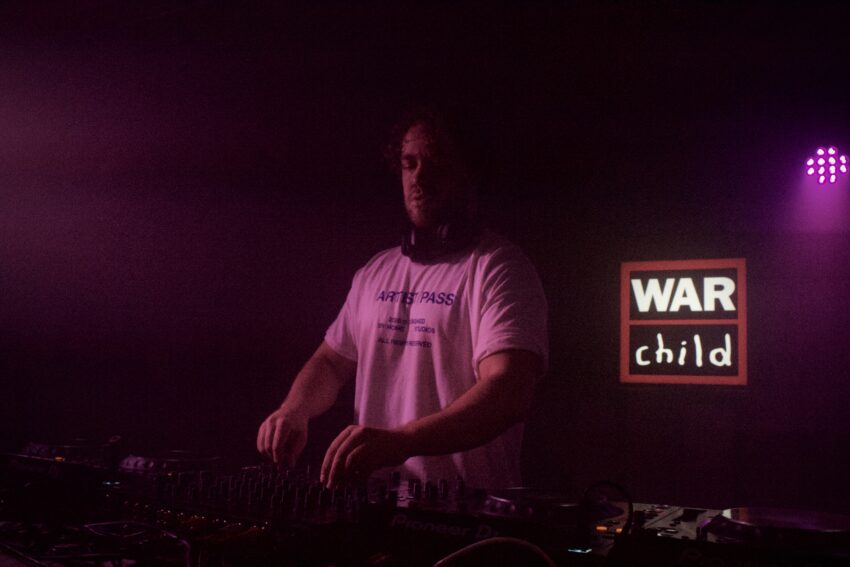 DJ performing under pink lighting at BRITs Week 2026 Manchester in YES Pink Room with War Child logo illuminated in the background.